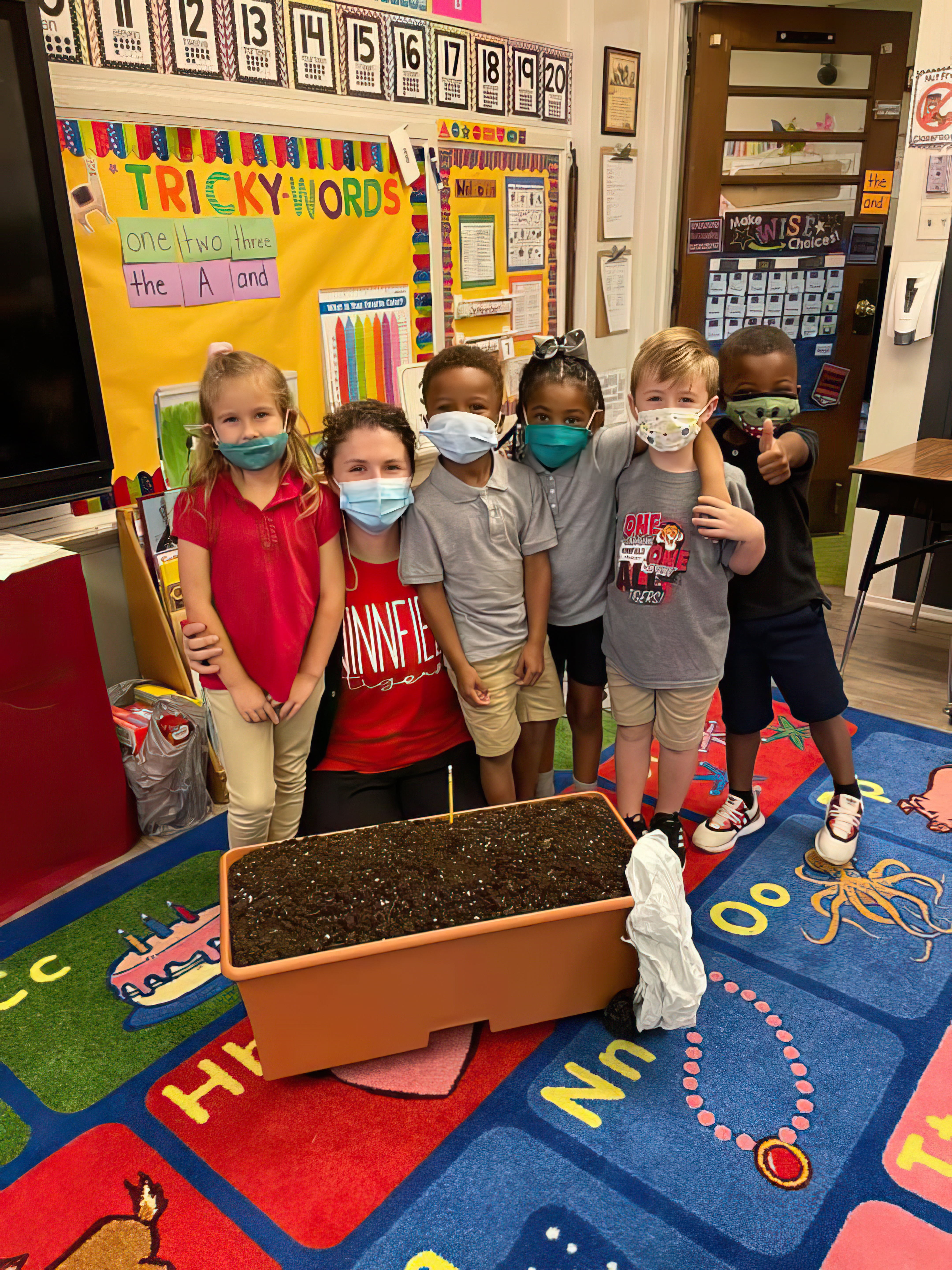 A teacher poses with five students as they set up a container garden set. 